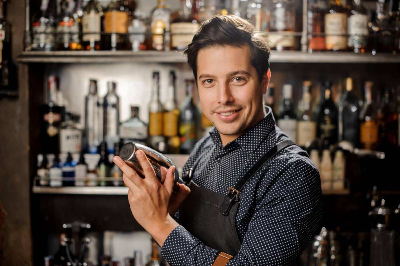 Handsome and young smiling brown haired barman with a shaker